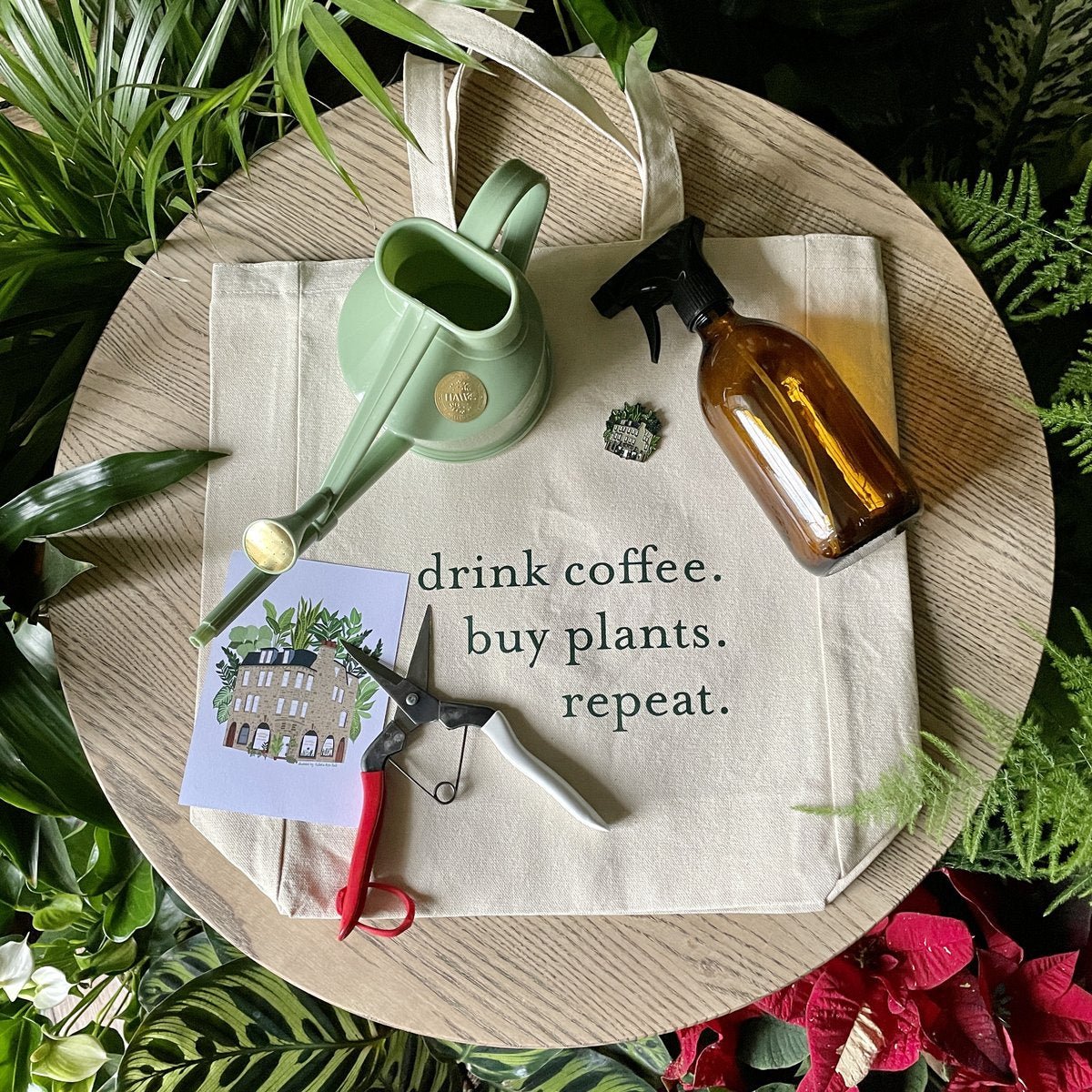 A glass mister, watering can, plant snips, tote bag and postcard on display in a plant shop.