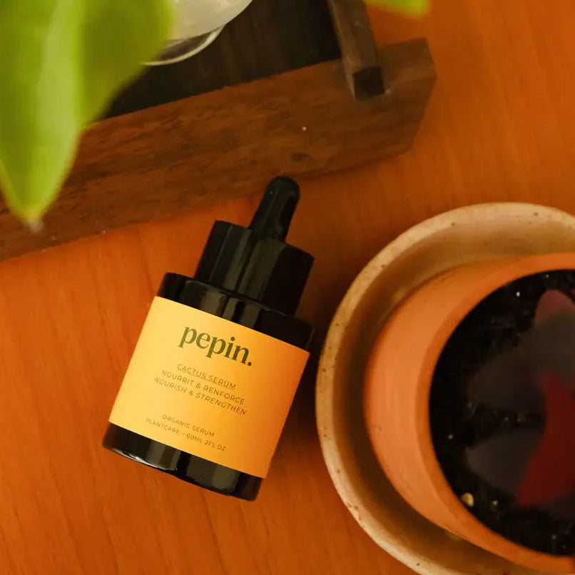 Pepin Cactus serum bottle on a wooden surface with a plant in the background