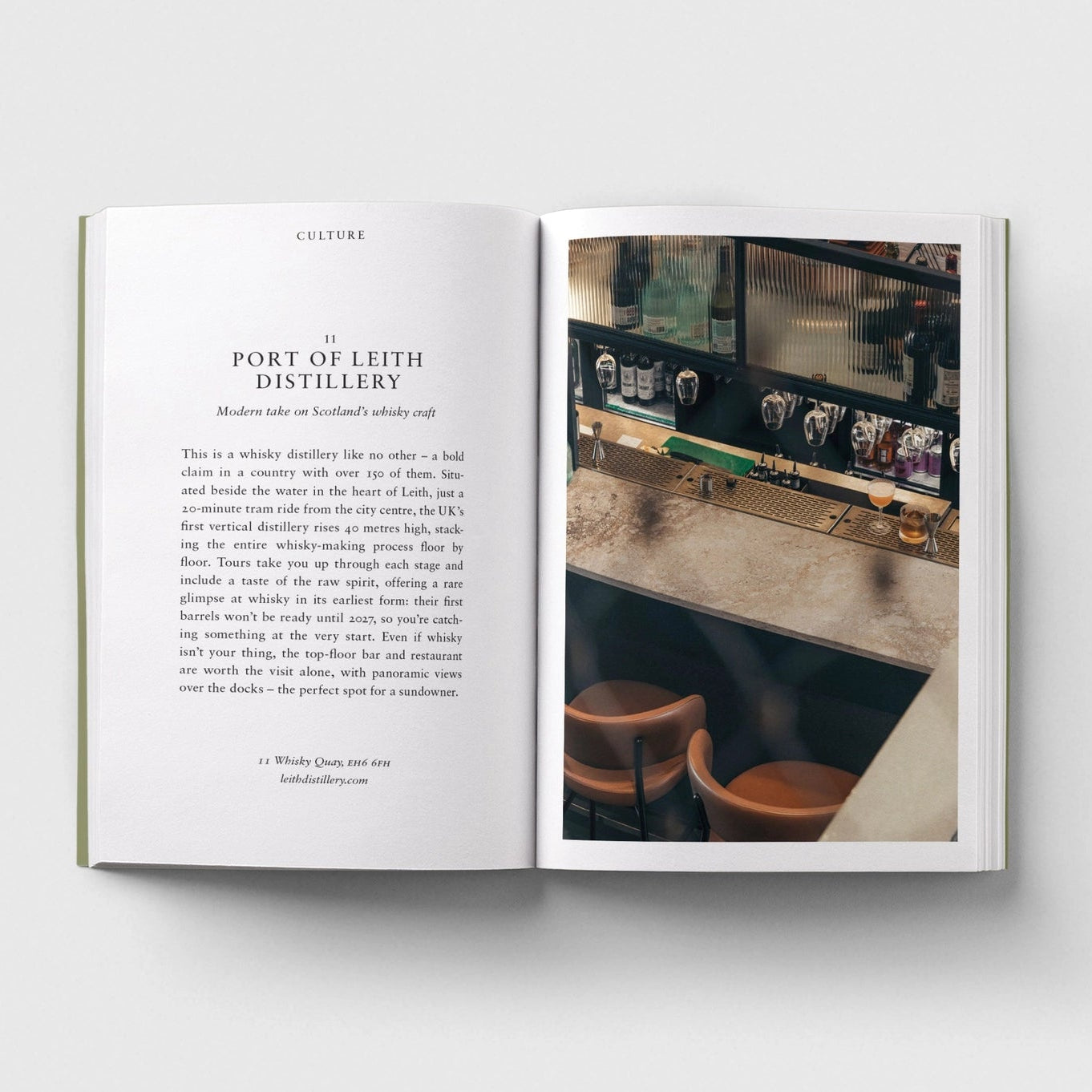 An open book laid flat on a light gray background. The left page contains a text article titled "Port of Leith Distillery" with a small inset photo, and the right page shows a photograph of a distillery interior with barrels and a wooden floor.