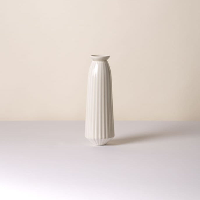 A tall, slender white ceramic Bergs Potter Cove watering spikeswith vertical fluted ridges, standing on a light gray surface against a warm beige background.