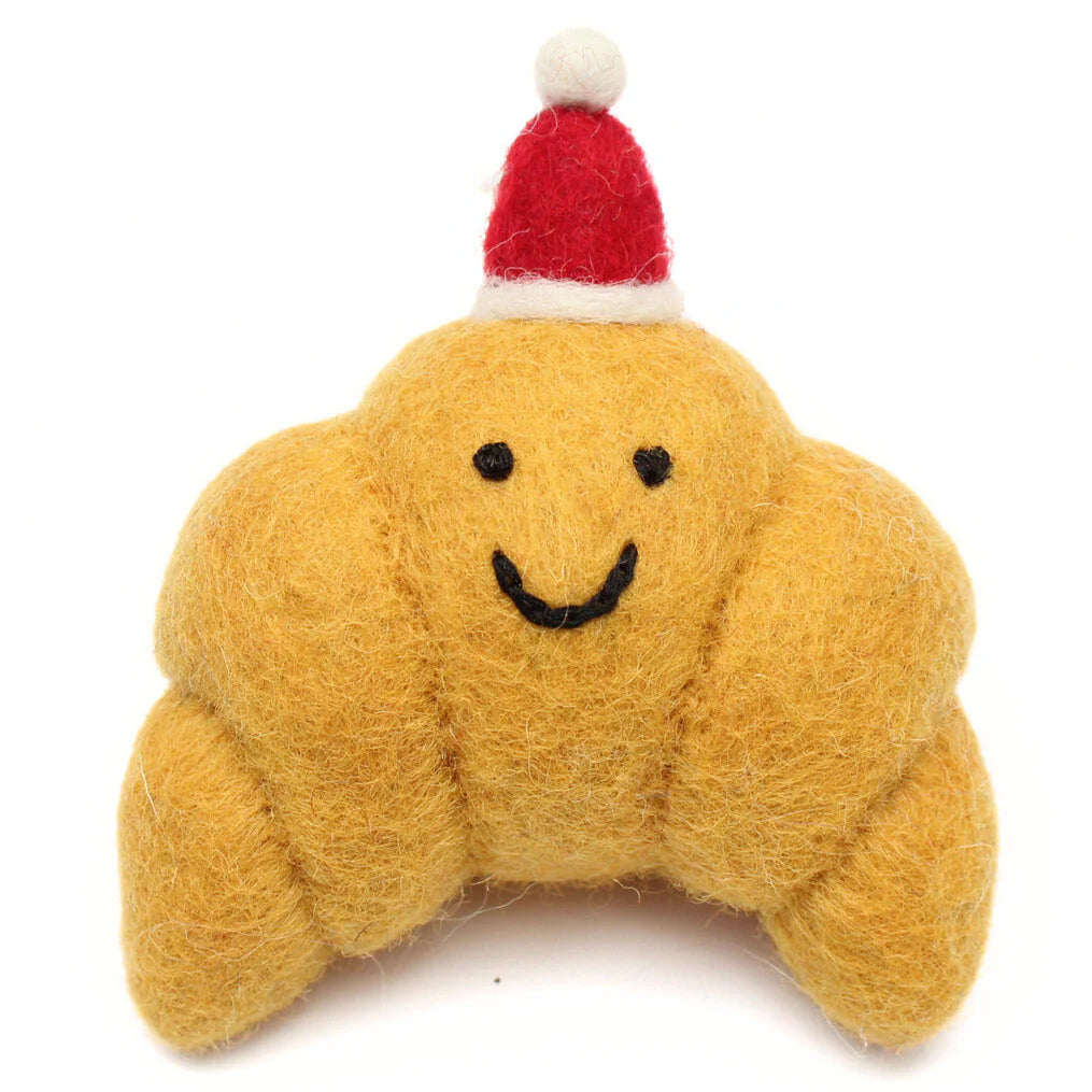 Yellow plush Croissant toy with a smiley face and red Santa hat on a white background
