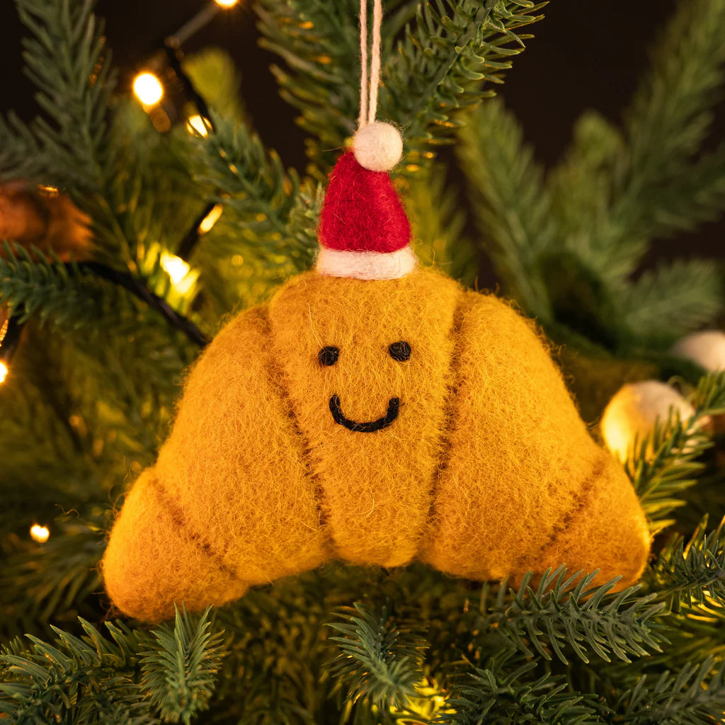 Felted yellow Croissant ornament with a Santa hat on a Christmas tree.