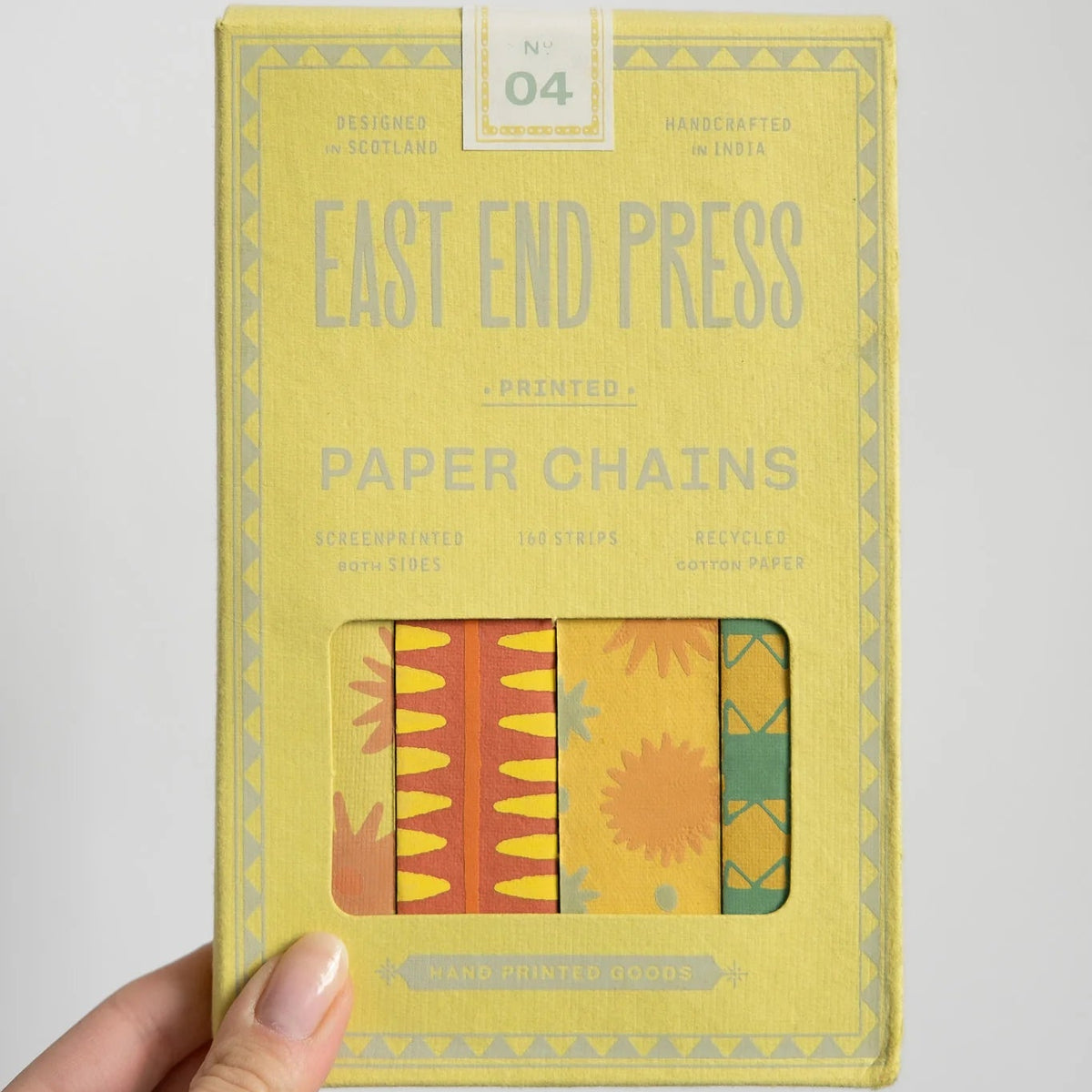 Yellow box of East End Press paper chains held by a hand against a light gray background