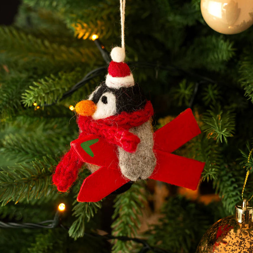 Decorative penguin ornament with a red scarf and Santa hat hanging on a Christmas tree.
