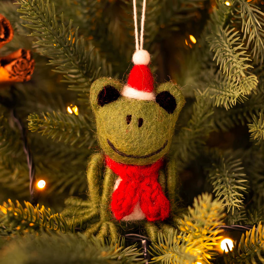 Felt frog ornament with a Santa hat and red scarf hanging on a Christmas tree.