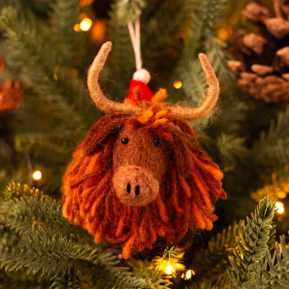 Yarn-braided Highland cow ornament on a Christmas tree with lights and pinecones.