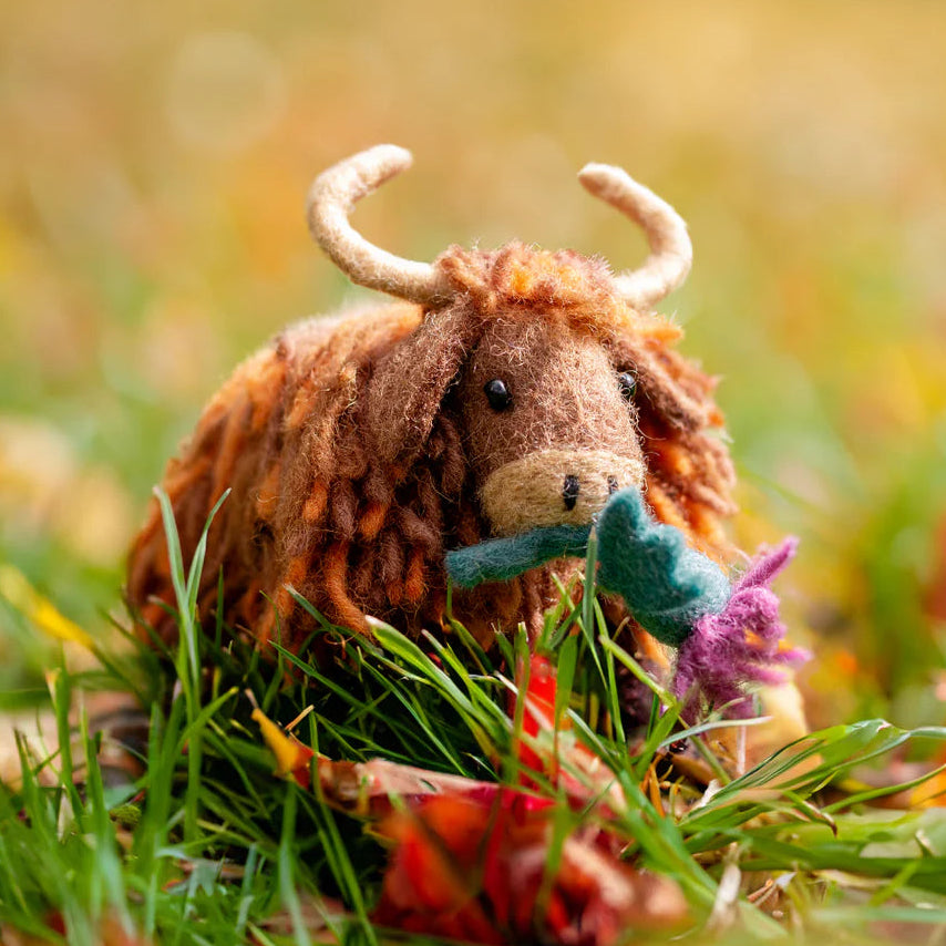 Plush toy cow sitting in a grassy field with flowers
