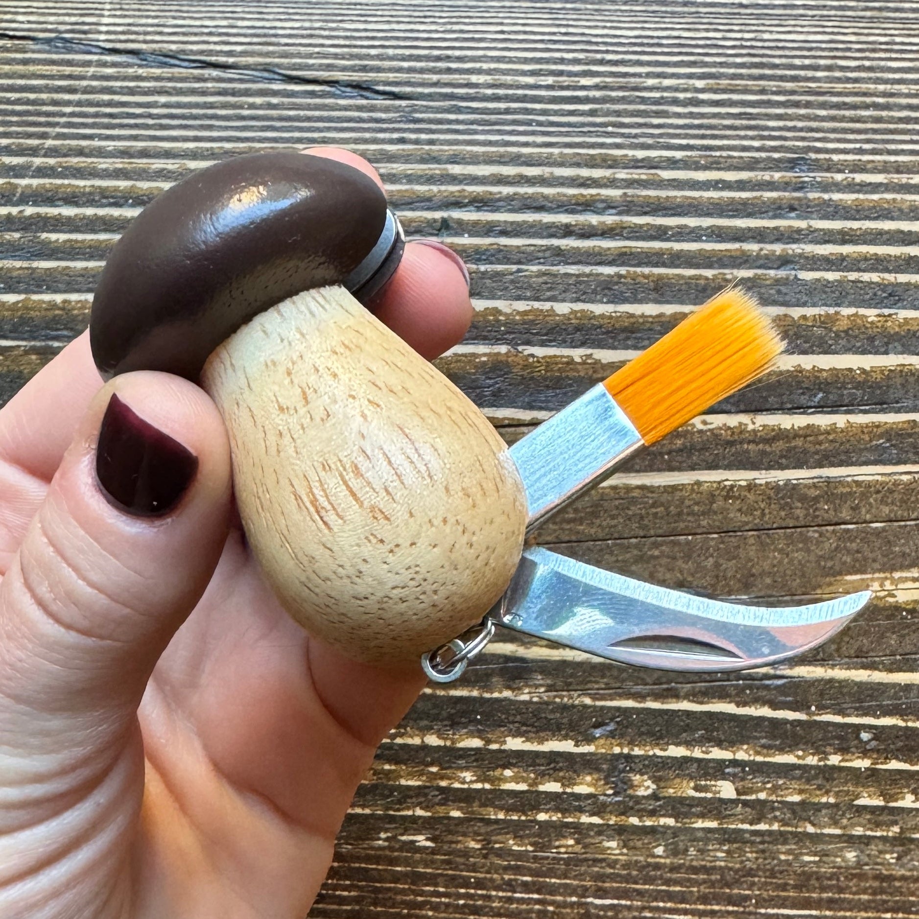 Multitool shaped like a mushroom with a brush and knife on a wooden surface