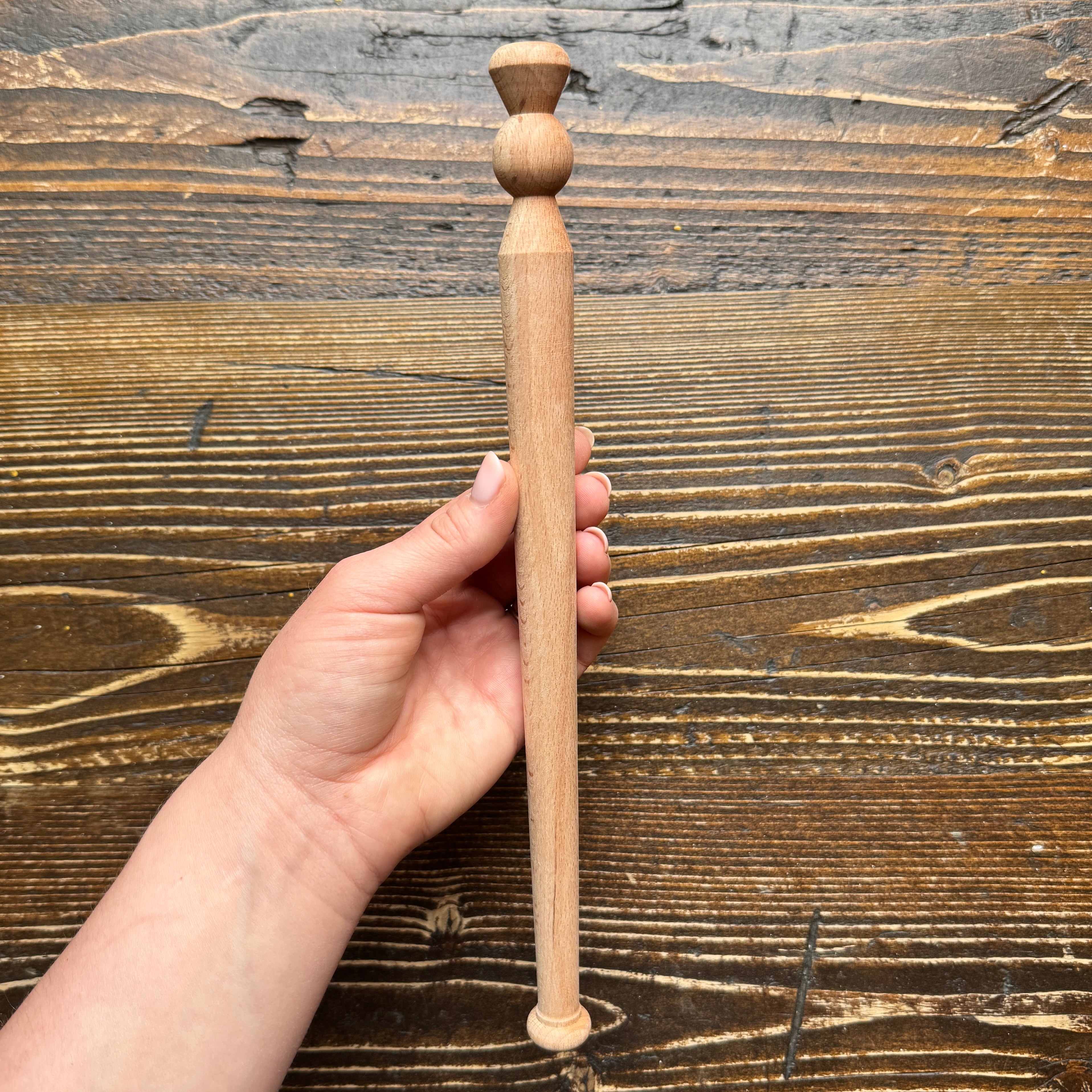 Hand holding a wooden porridge spurtle against a wooden background