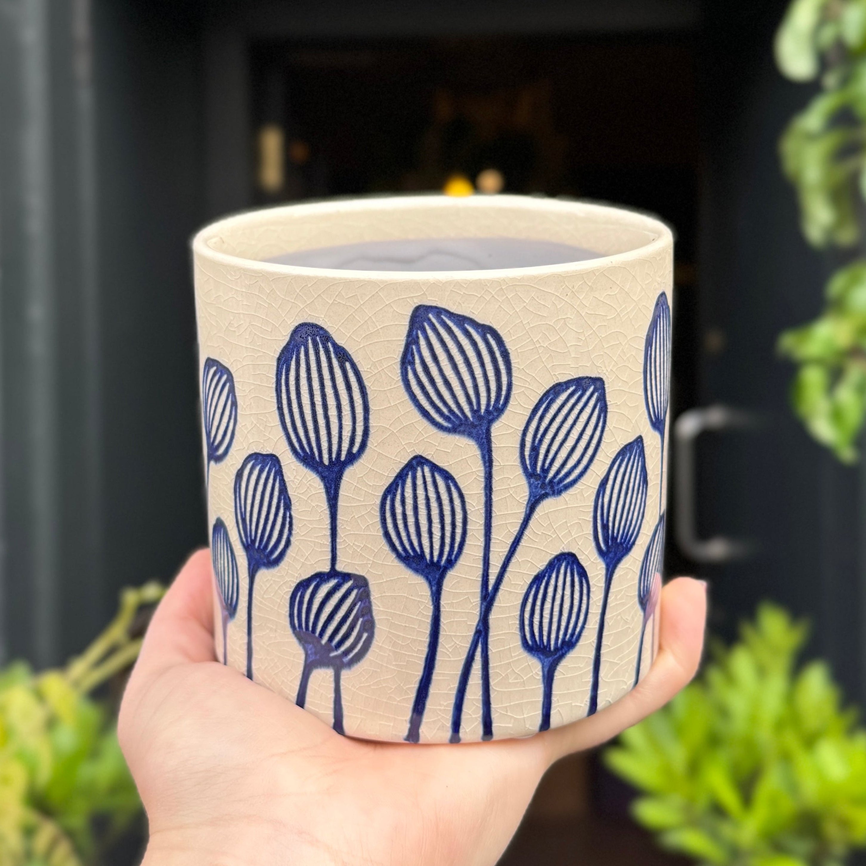 Hand holding a ceramic plant pot with blue floral patterns against a blurred indoor background