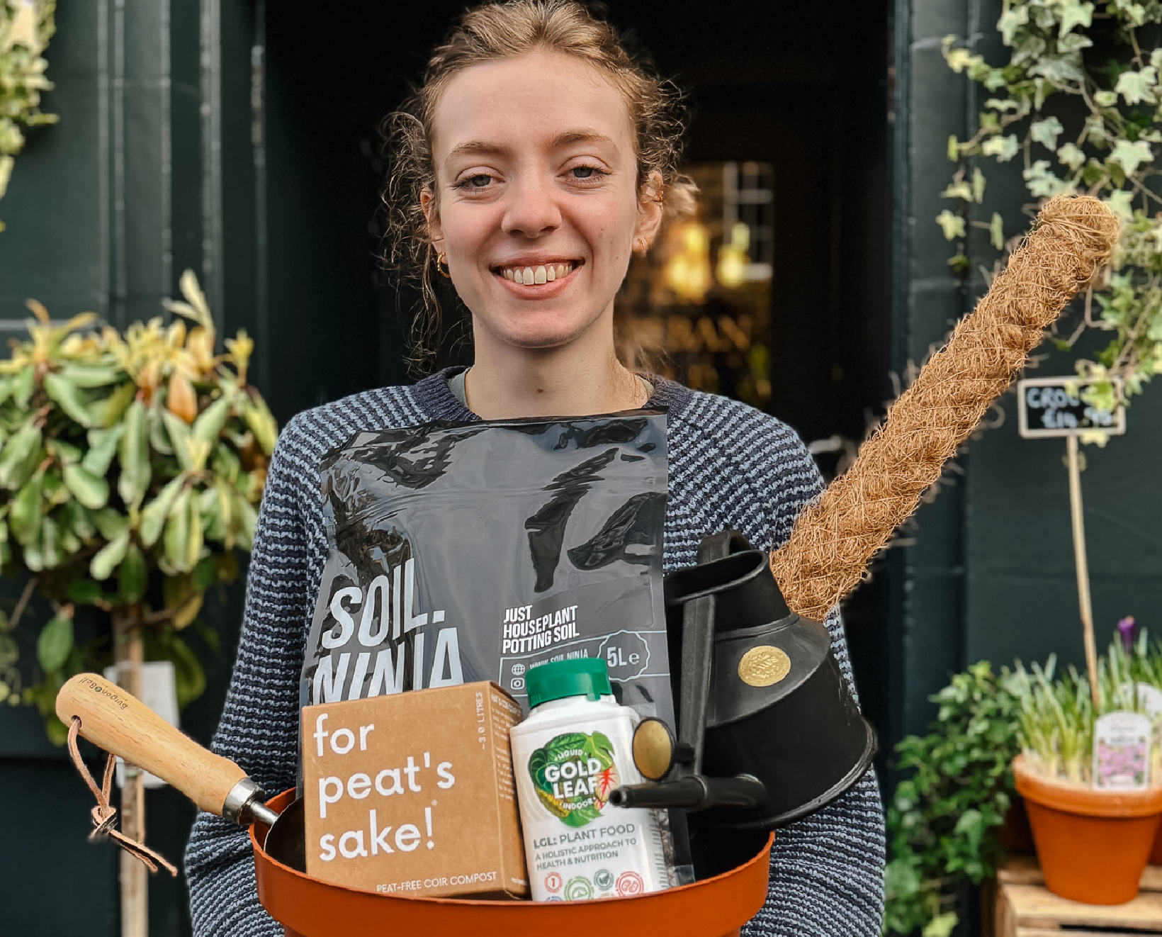 Woman outside grow urban. holding indoor plant repotting essentials including compost, plant feed and watering can