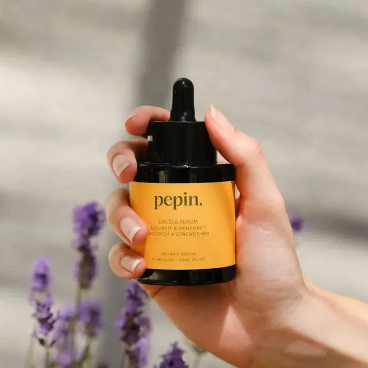 Hand holding a 'pepin' cactus serum bottle with lavender flowers in the background