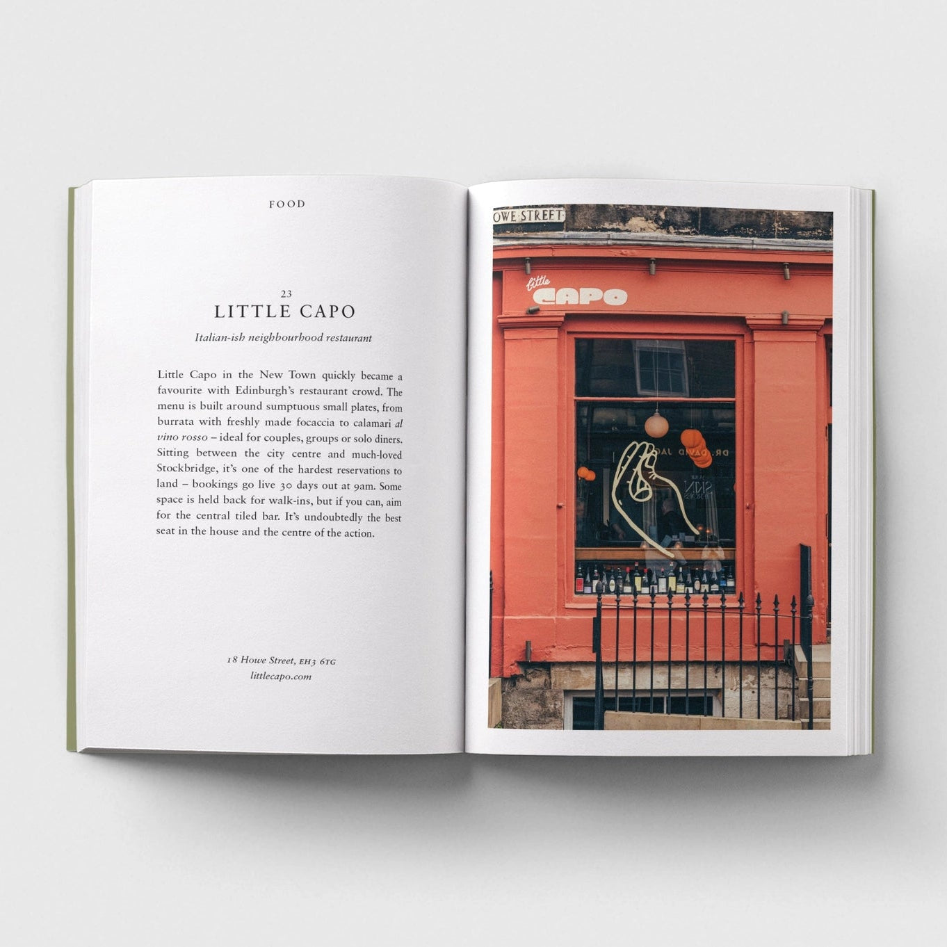 An open book laid flat on a light grey background, showing a printed interior page with text on the left and a colour photograph of the red frontage of Little Capo in Edinburgh.