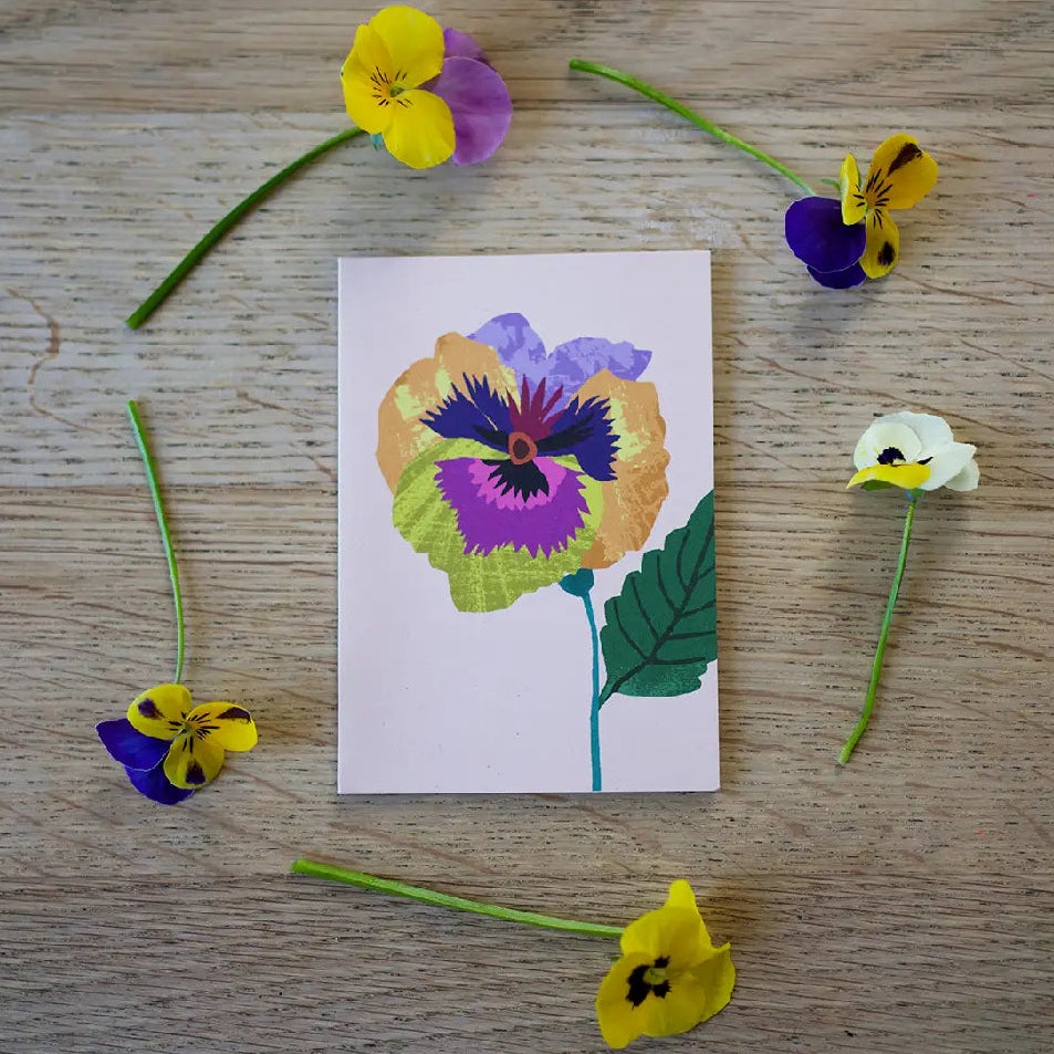 Card with a colorful flower design surrounded by small flowers on a wooden surface