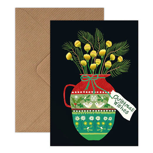 A Christmas-themed greeting card with a brown envelope, featuring an illustration of yellow mimosa flowers in a red and green patterned vase on a black background, with a white tag reading 'Christmas Wishes'.