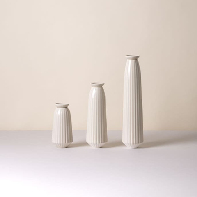 Three white ceramic Bergs Potter Cove watering spikes of different sizes on a light surface with a beige background.