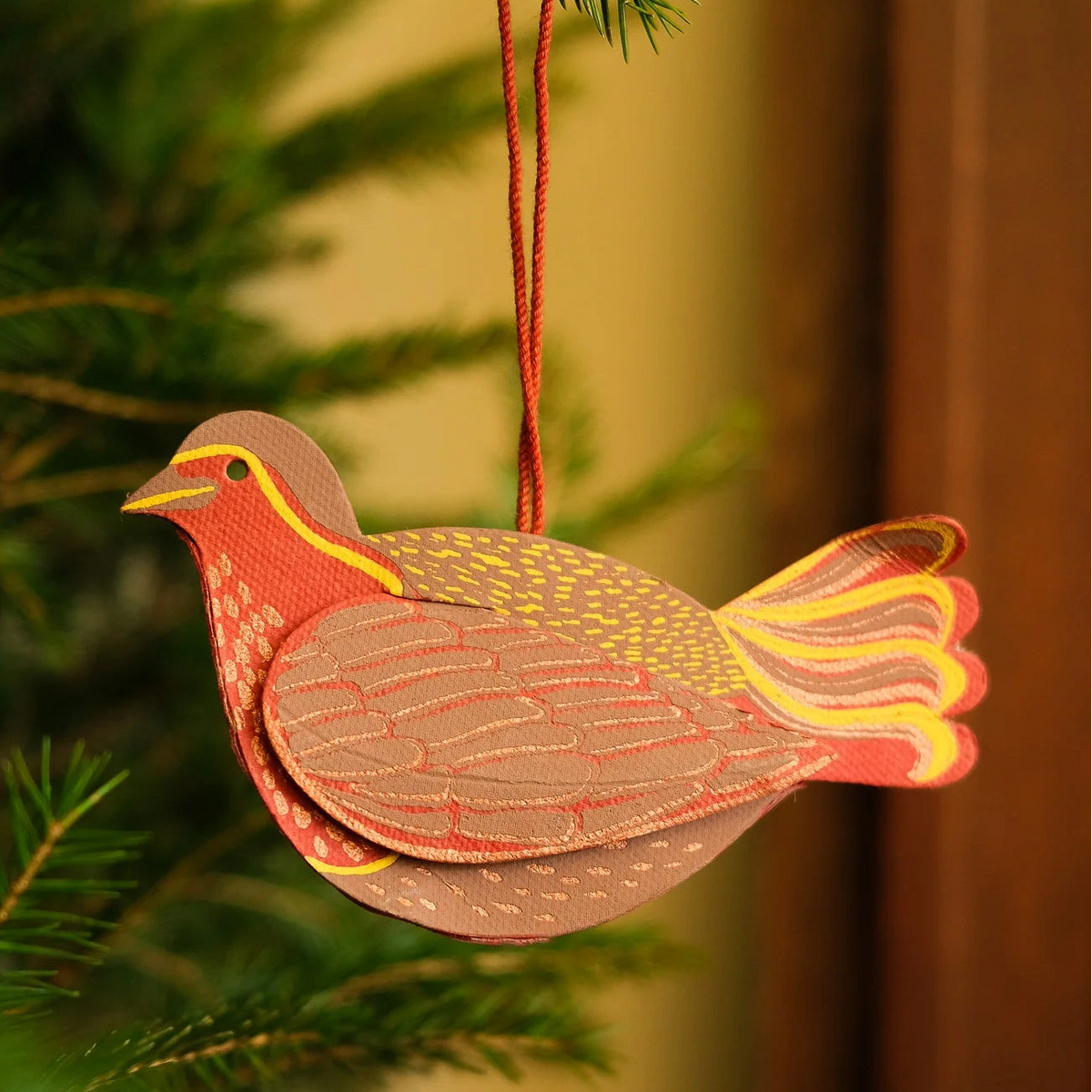 Decorative bird ornament hanging on a Christmas tree branch.