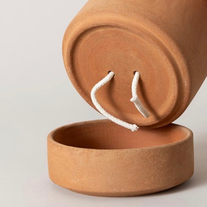 A terracotta clay Bergs Viva plant pot with a matching round base, shown with the top tilted over the base to reveal two white wicks.