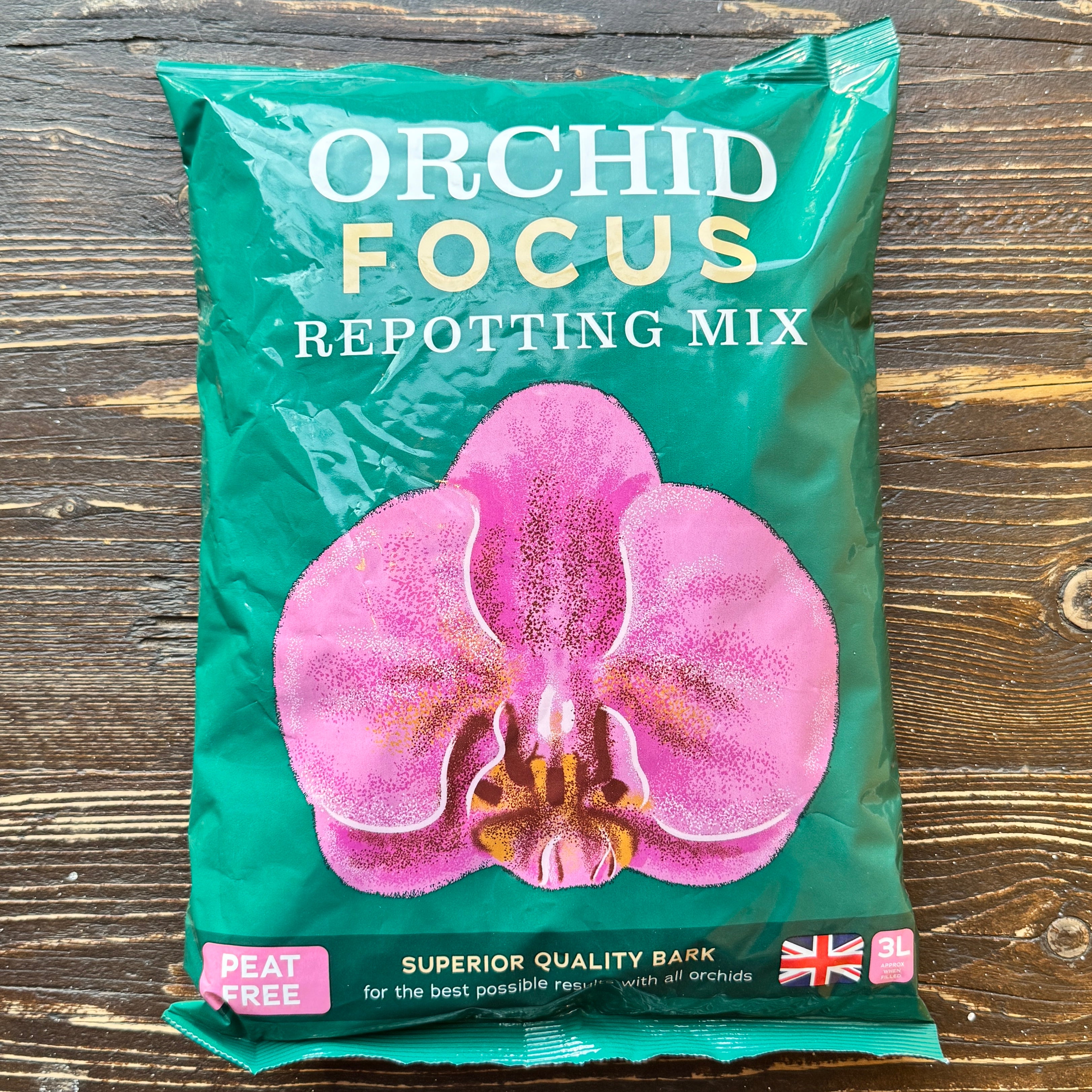 Bag of Orchid Focus repotting mix with a pink orchid on a wooden surface