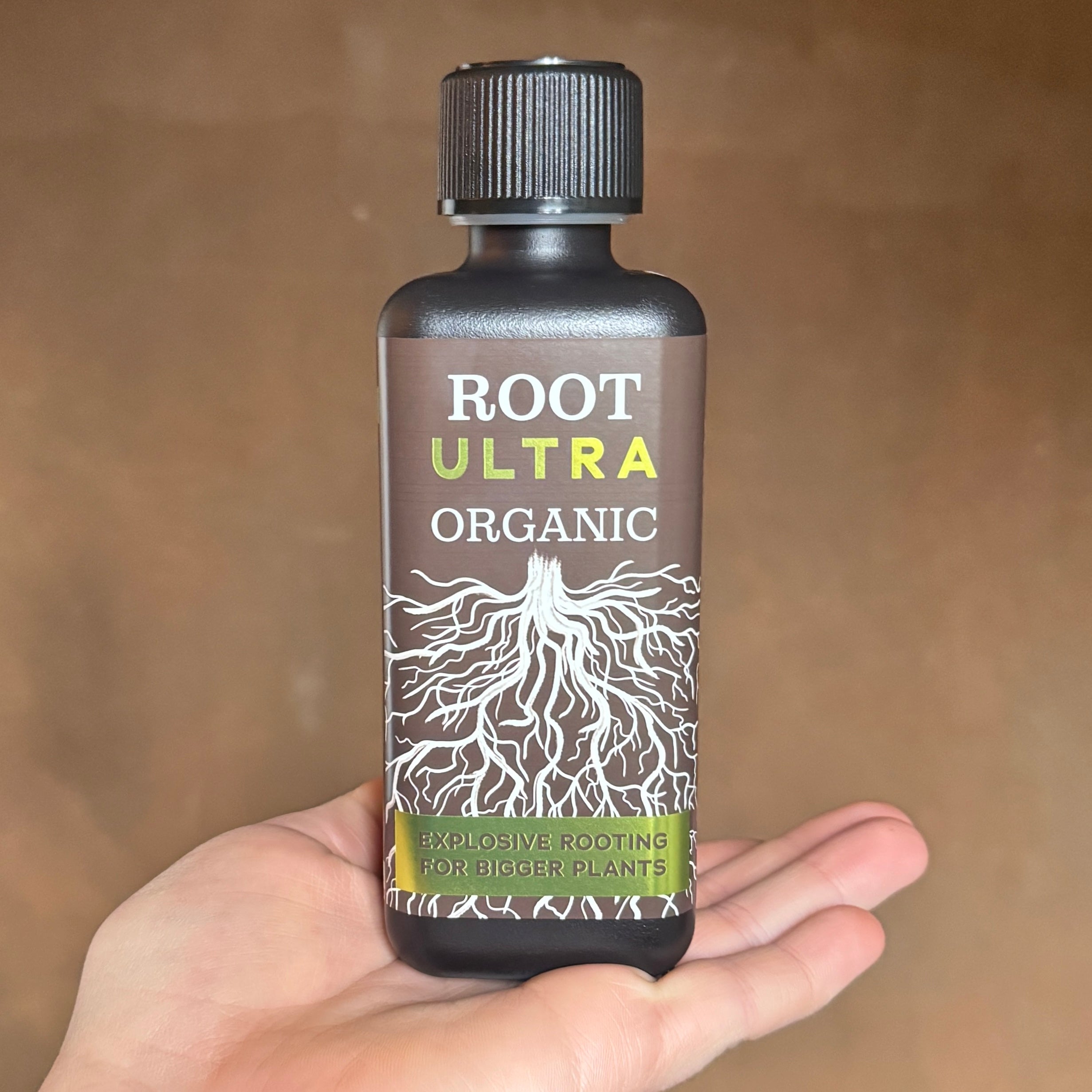 Bottle of Root Ultra Organic plant growth supplement held in a hand against a brown background