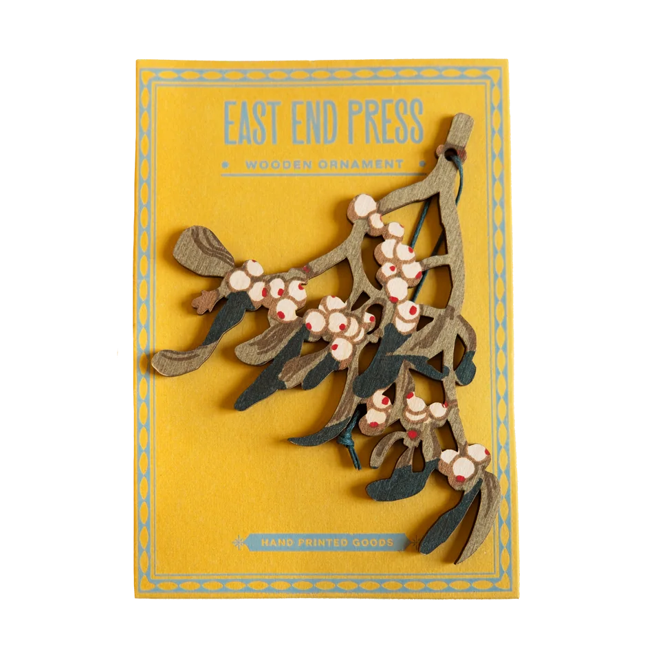 Illustrated mistletoe wooden decoration with pink berries and green leaves, with the text 'EAST END PRESS' at the top, shown on a plain white background.