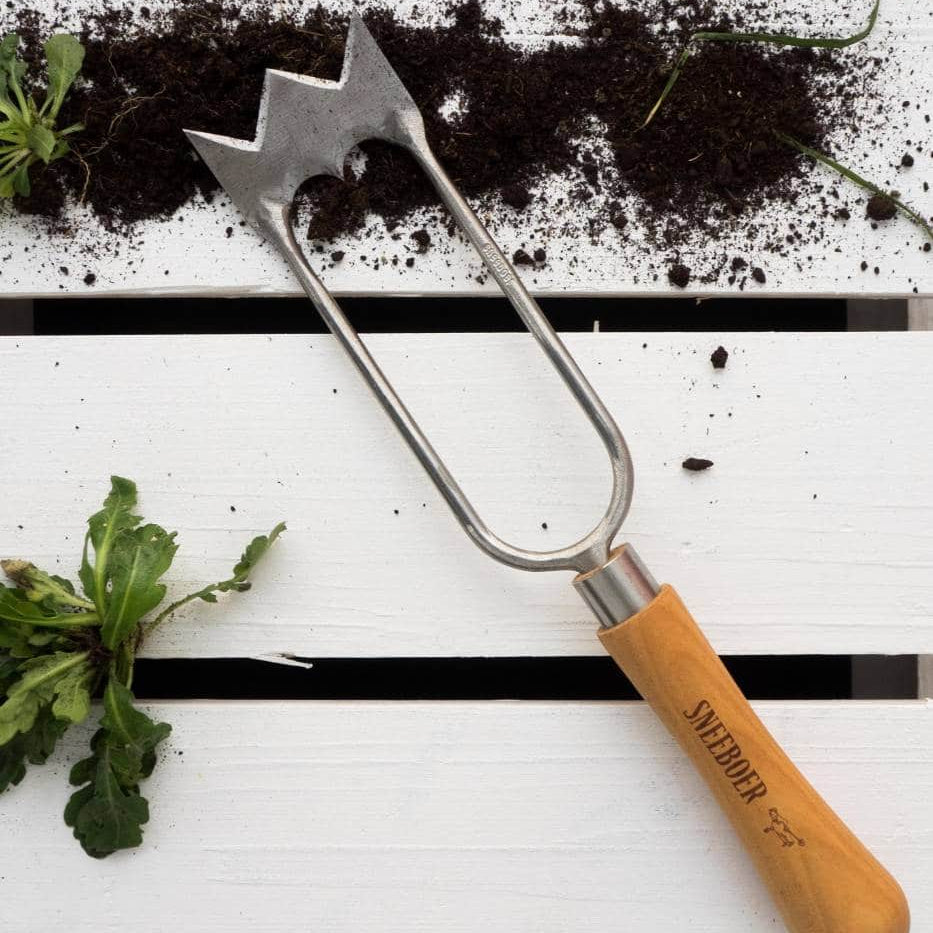 Sneeboer Royal Dutch Hand Hoe garden tool with wooden handle on a white surface with soil and plants.