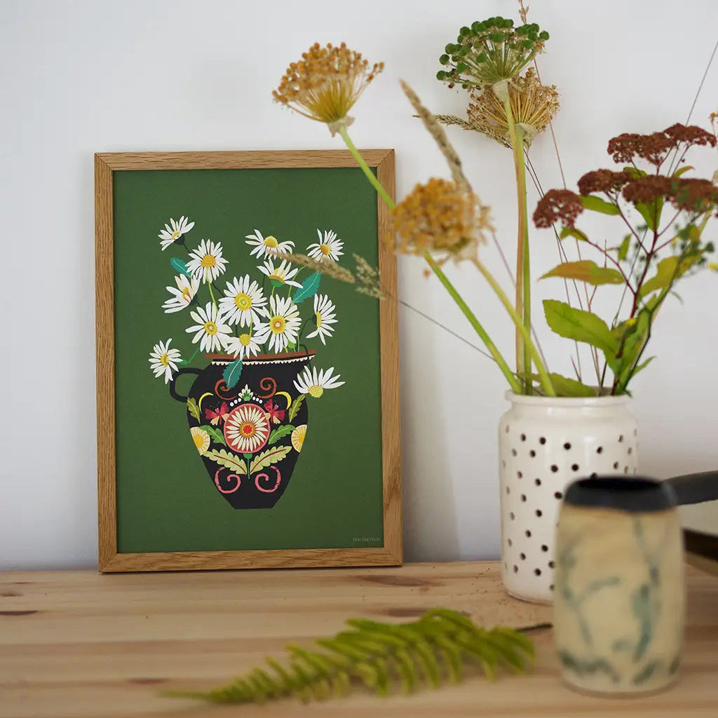 Framed artwork of a floral design on a wooden surface with a vase and plants.