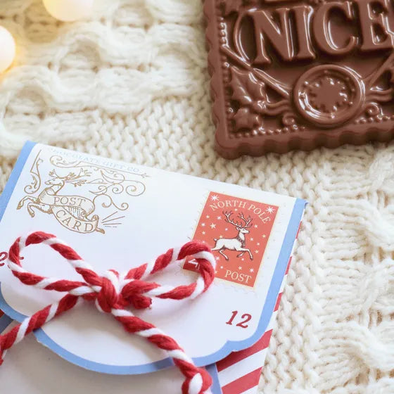 A chocolate gift card wrapped in red and white twisted cord, placed on a cream cable-knit blanket next to a chocolate bar with a 'Nice' embossing.