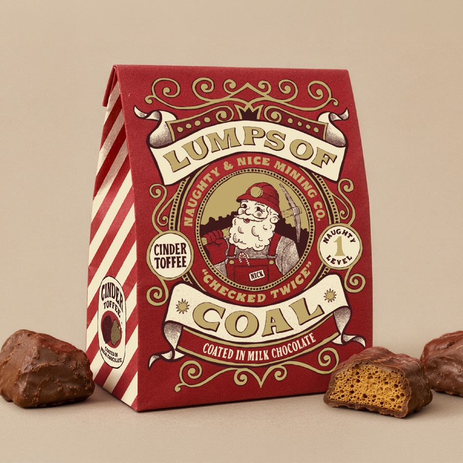 A red and white striped bag of Lumps of Coal coated in milk chocolate, shown with chocolate chunks on a beige background.