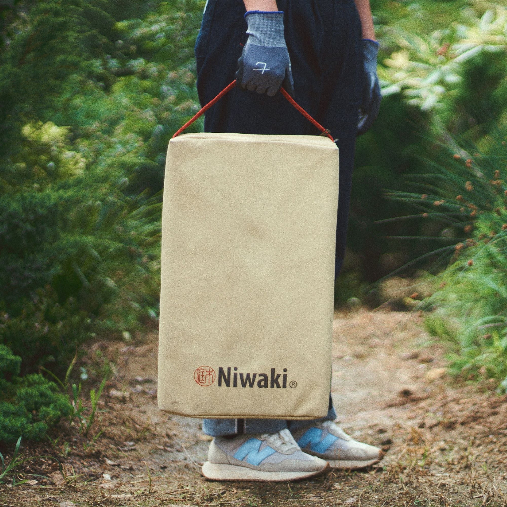 Person holding a tan gardening kneeler mat with 'Niwaki' branding in a garden setting