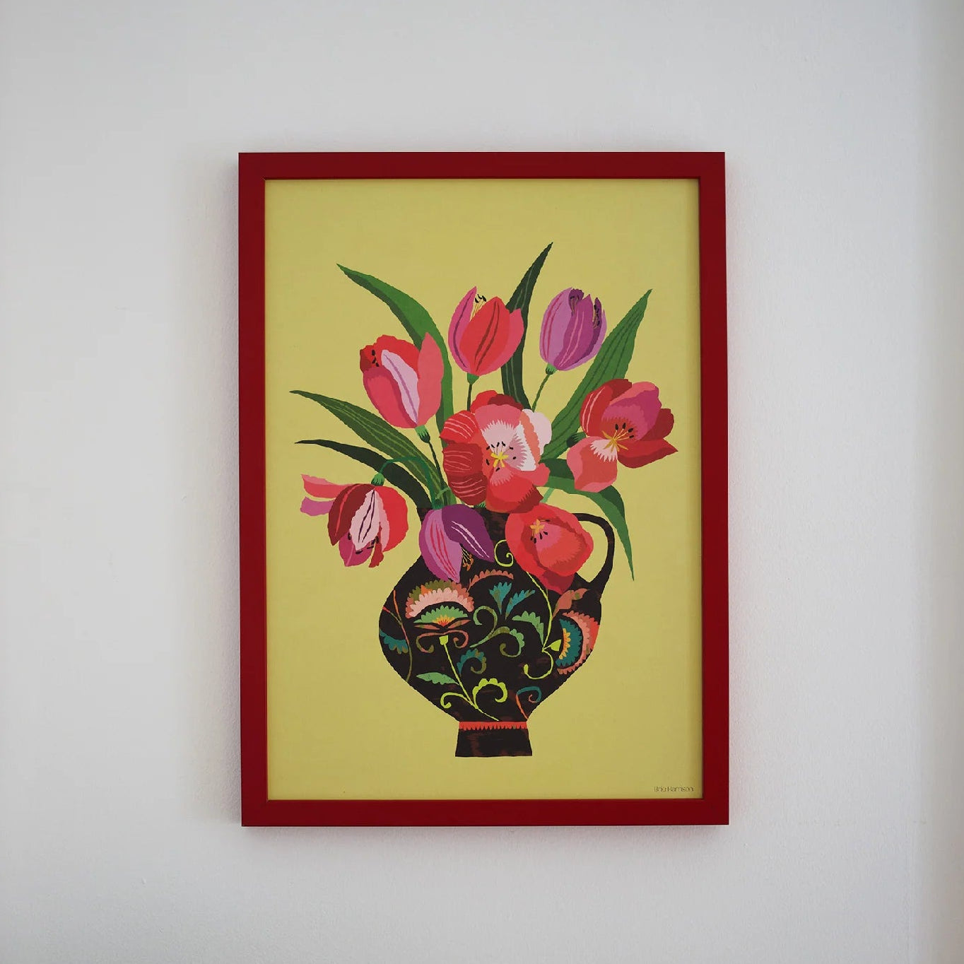 Framed artwork of flowers on a wall above a wooden table with a bowl of fruit.