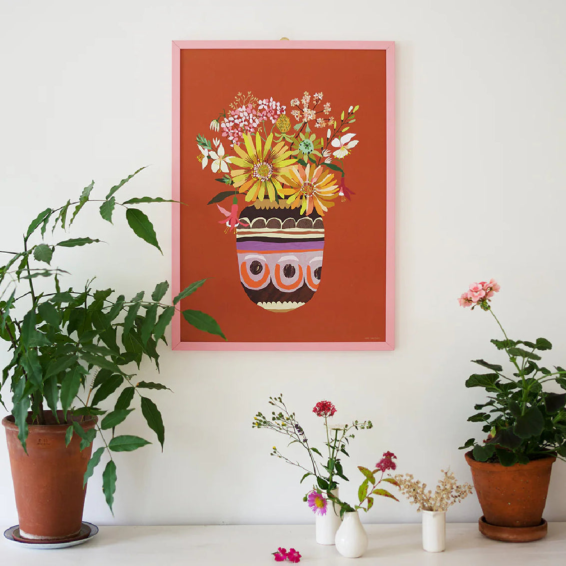 Framed floral artwork on a wall with potted plants below